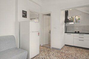 A compact kitchen with a refrigerator, a sink, and a stove. There is a door leading to another room.