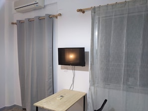 Habitació amb televisió penjada, taula de fusta i cortines.
