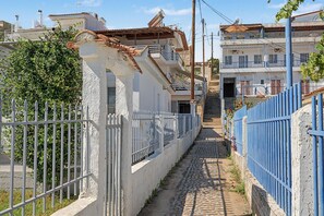 Una estrecha calle adoquinada bordeada por edificios blancos con barandillas azules y una valla blanca.