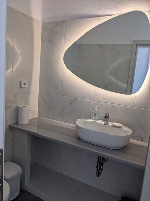 A bathroom with a marble-tiled wall, a white sink with a soap dispenser, and a toilet. - Apartment 'Kagias  2' with Sea View, Wi-Fi and Air Conditioning (Petalidi)