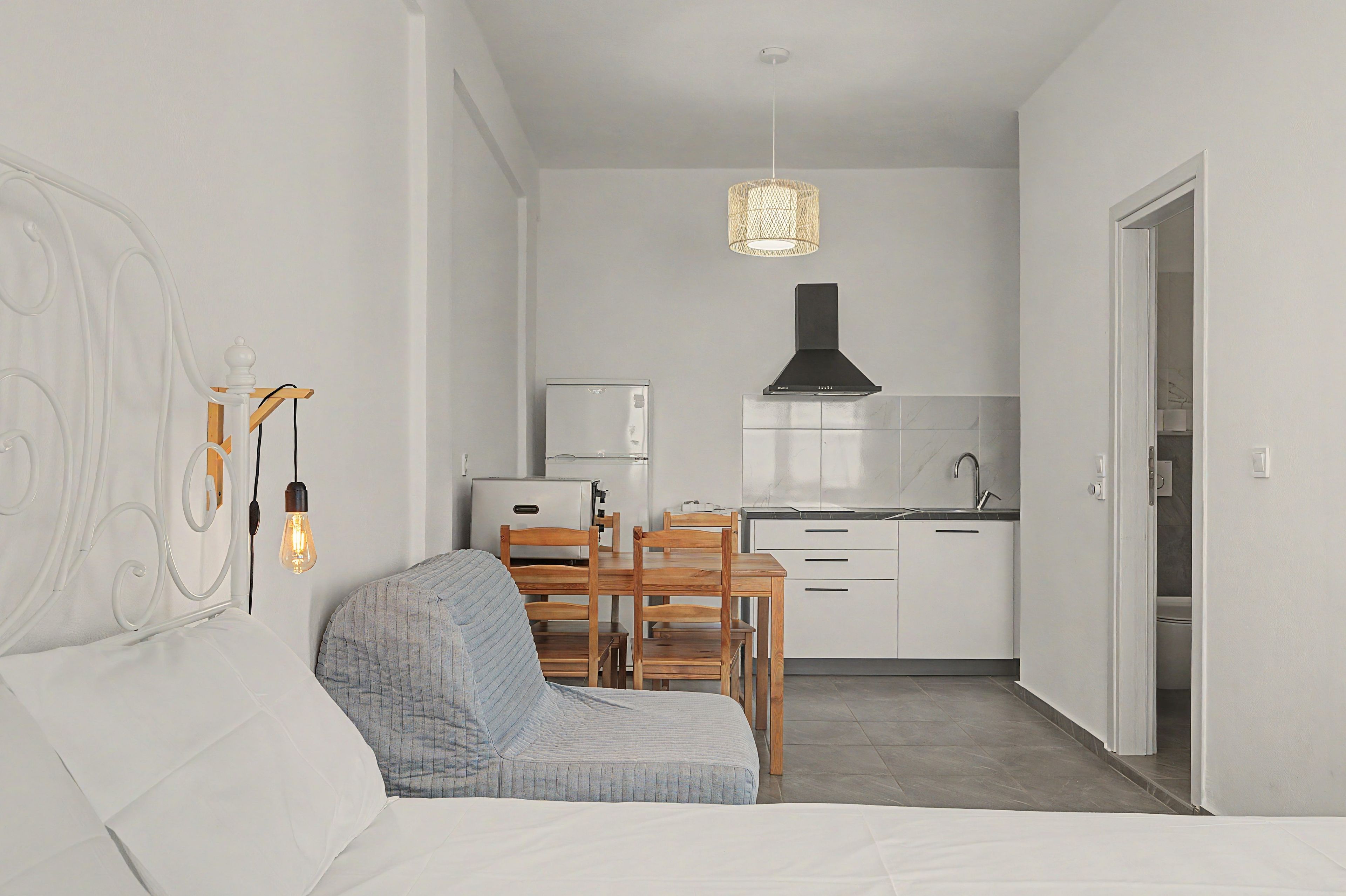 A compact living space with a bed, a dining table with chairs, a kitchenette, and a hanging light fixture.