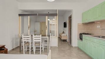 A room with a bed, a dining table with chairs, a kitchen with green cabinets, and a hallway leading to another room.