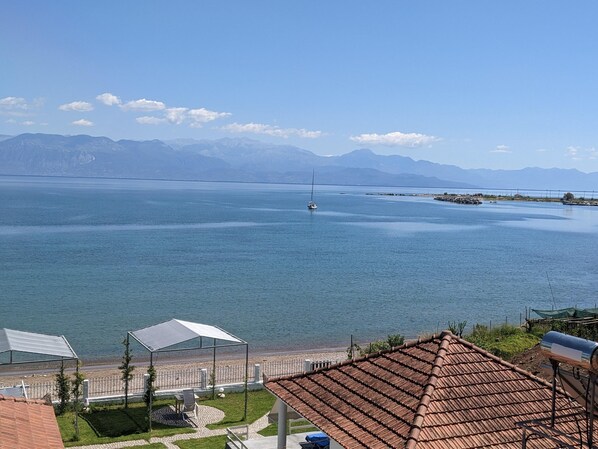 A coastal view with a clear sky, a body of water, distant mountains, and a building with a tiled roof.