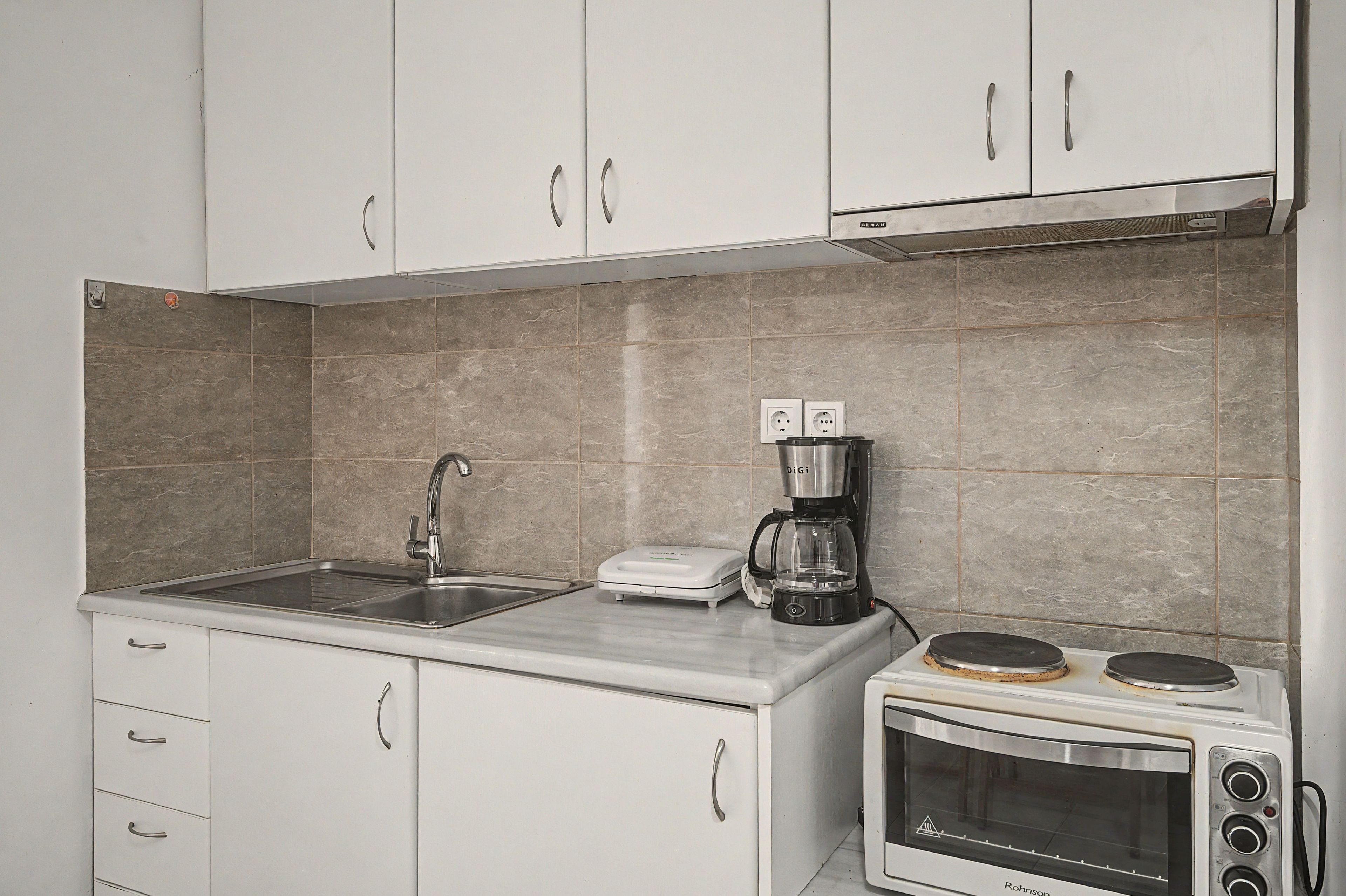 A kitchen with white cabinets, a sink, a coffee maker, and a toaster oven.