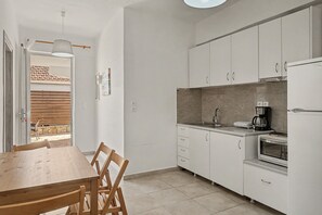 A compact kitchen with white cabinets, a wooden dining table, and a built-in oven. - Apartment 'Kagias  4' with Sea View, Wi-Fi and Air Conditioning (Petalidi)