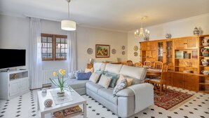Een woonkamer met een bank, salontafel, televisie en een eetgedeelte met stoelen en een kast.