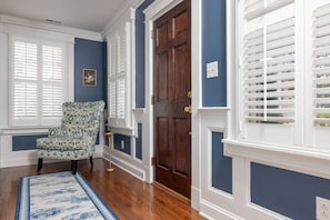 A room with a patterned armchair, a wooden door, and a window with shutters. - 5BR Historic Downtown (Edenton)