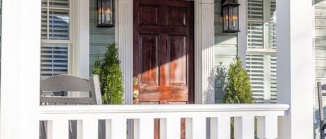 A porch with a wooden door, white railings, and two lanterns.