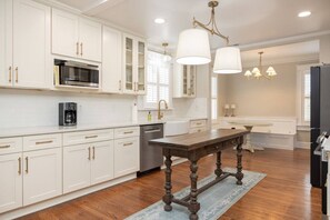 A kitchen with white cabinetry, a coffee maker, a dishwasher, and a wooden table with a rug. - 5BR Historic Downtown (Edenton)