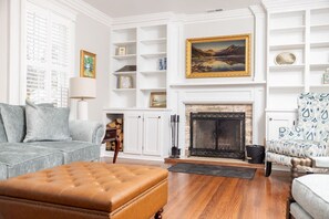 A living room with a fireplace, a sofa, a patterned armchair, and a wooden coffee table. - 5BR Historic Downtown (Edenton)