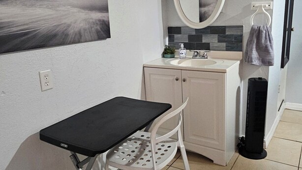 Una habitación pequeña y limpia con escritorio, silla y un espejo grande.