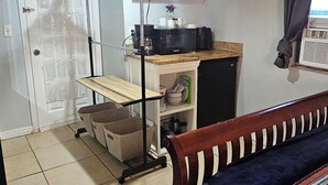 Un dormitorio con una cama, un escritorio con computadora, un televisor y un tendedero.