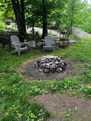 En trädgård med två Adirondack-stolar, en eldstad och en stenmur.