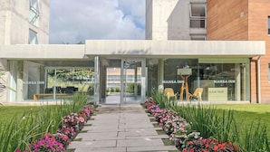 Un edificio moderno con entrada de vidrio, identificado como 'Mansa Inn', y un camino que conduce a la entrada.