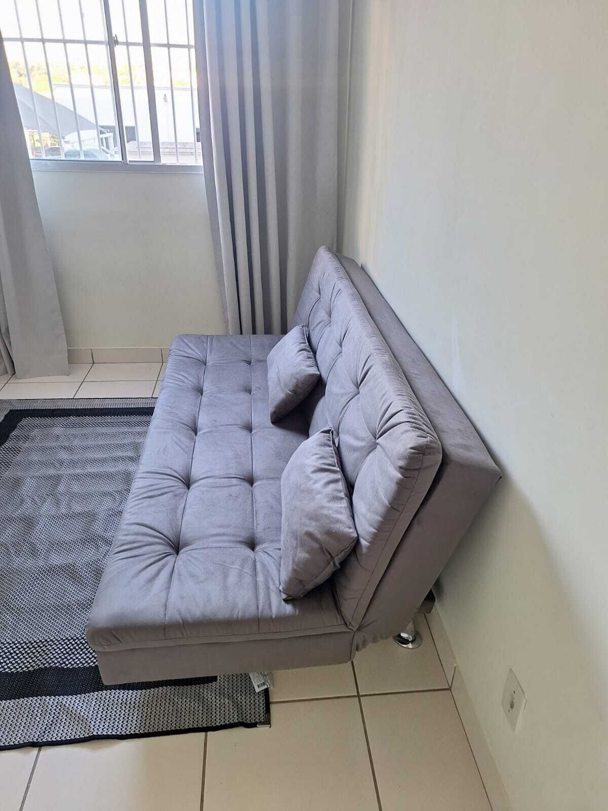 En hjørnesofa med pude, et sort-hvidt tæppe og et vindue med gardiner.