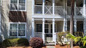 A two-story building with a porch, a covered entryway, and a small garden area with mulch and plants. - Enjoy beach life in a 3-bedroom condo in gorgeous Blue Mountain Beach on 30a. (Santa Rosa Beach)