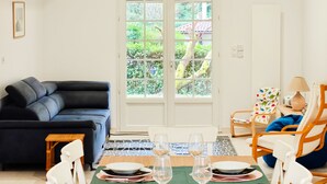 Un salon avec un canapé, une table à manger dressée pour deux personnes, une chaise et une lampe.