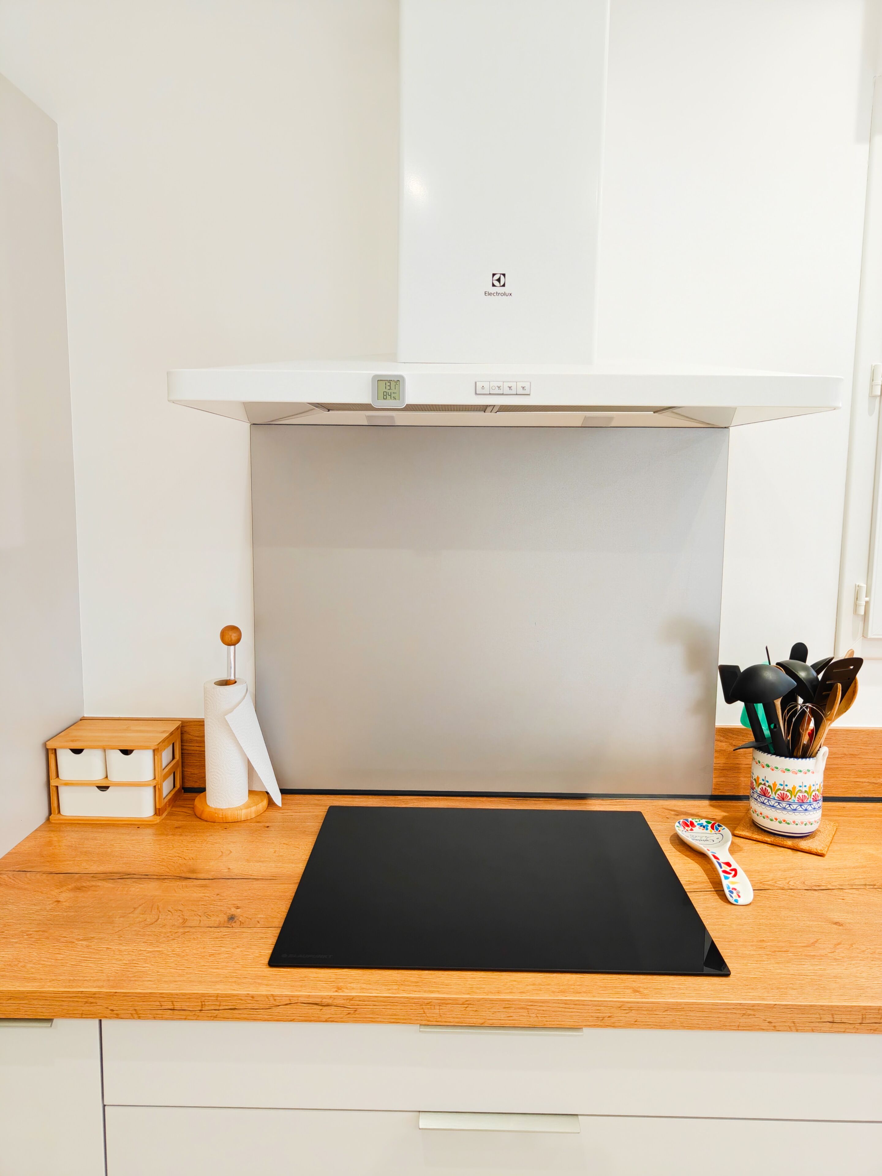 A kitchen with a white range hood, a black cutting board, a wooden storage box, a paper towel holder, and a utensil holder.