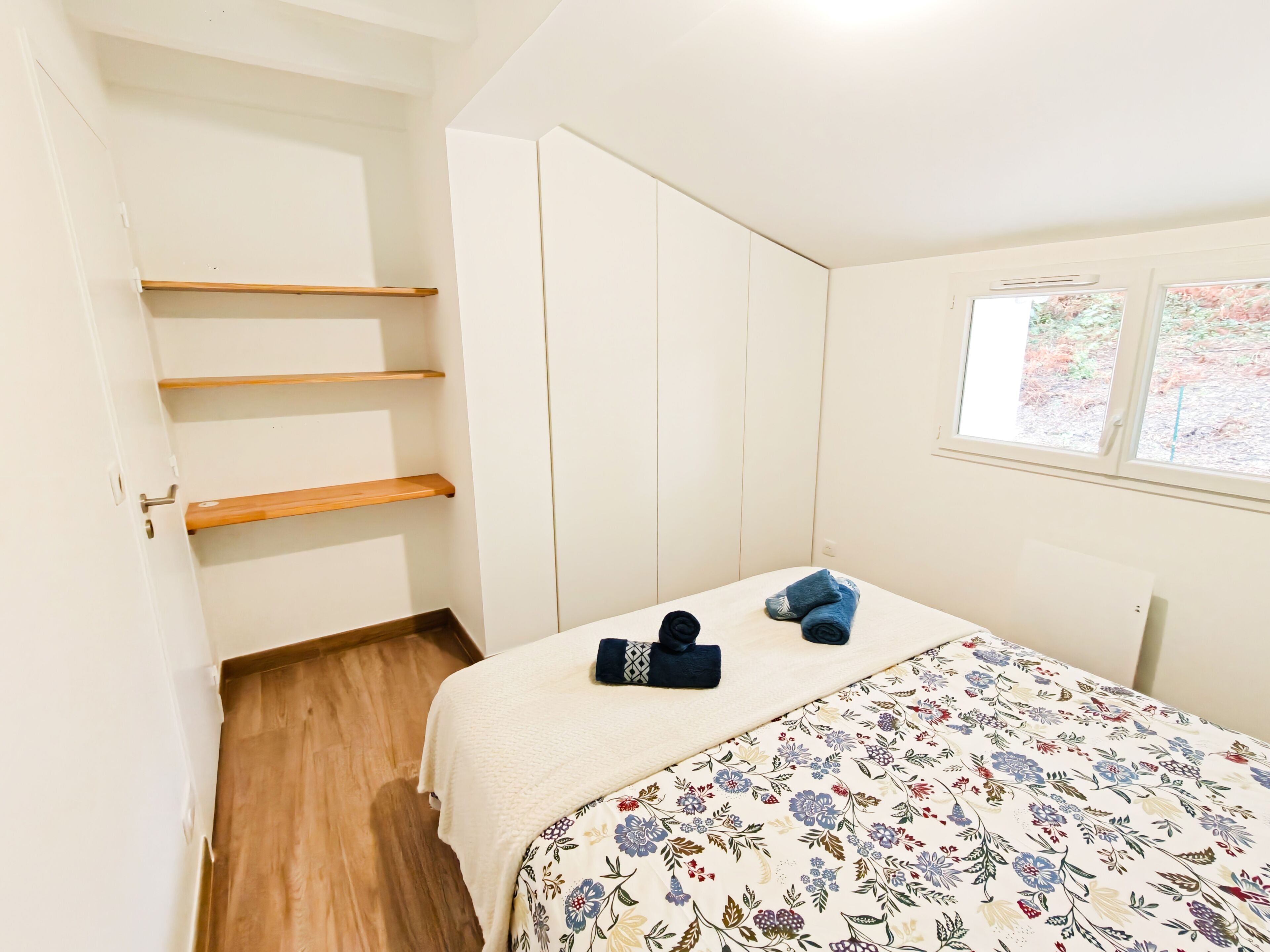 A bedroom with a bed, a wardrobe, a window with a view, and a door.