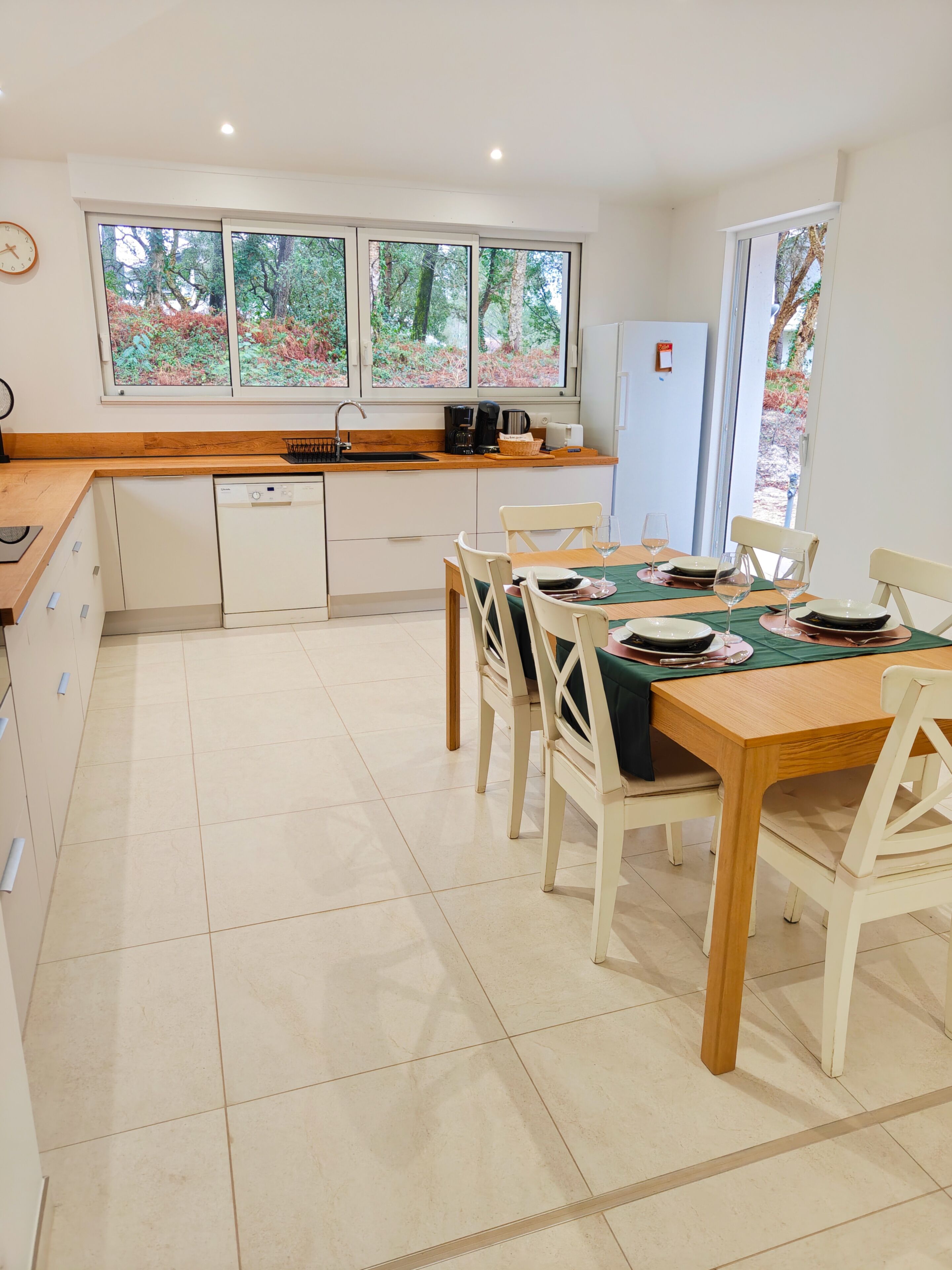 A modern kitchen with a dining area, large windows, and a dishwasher.