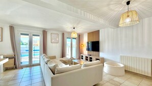 A modern living room with a sofa, TV, and a ceiling light fixture. - Le Jardin Bleu, 6-person villa swimming pool (Saint-Geniès-de-Malgoirès)