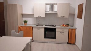 A compact kitchen with a gas stove, oven, and sink, a dining table with chairs, and a potted plant. - A retreat in the baroque heart of Ragusa Ibla (Ragusa)