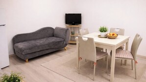 A living room with a sofa, a dining table with chairs, a television, and a small plant. - A retreat in the baroque heart of Ragusa Ibla (Ragusa)