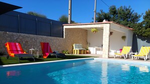 Una piscina con lettini, un muro in pietra e una zona patio coperta.