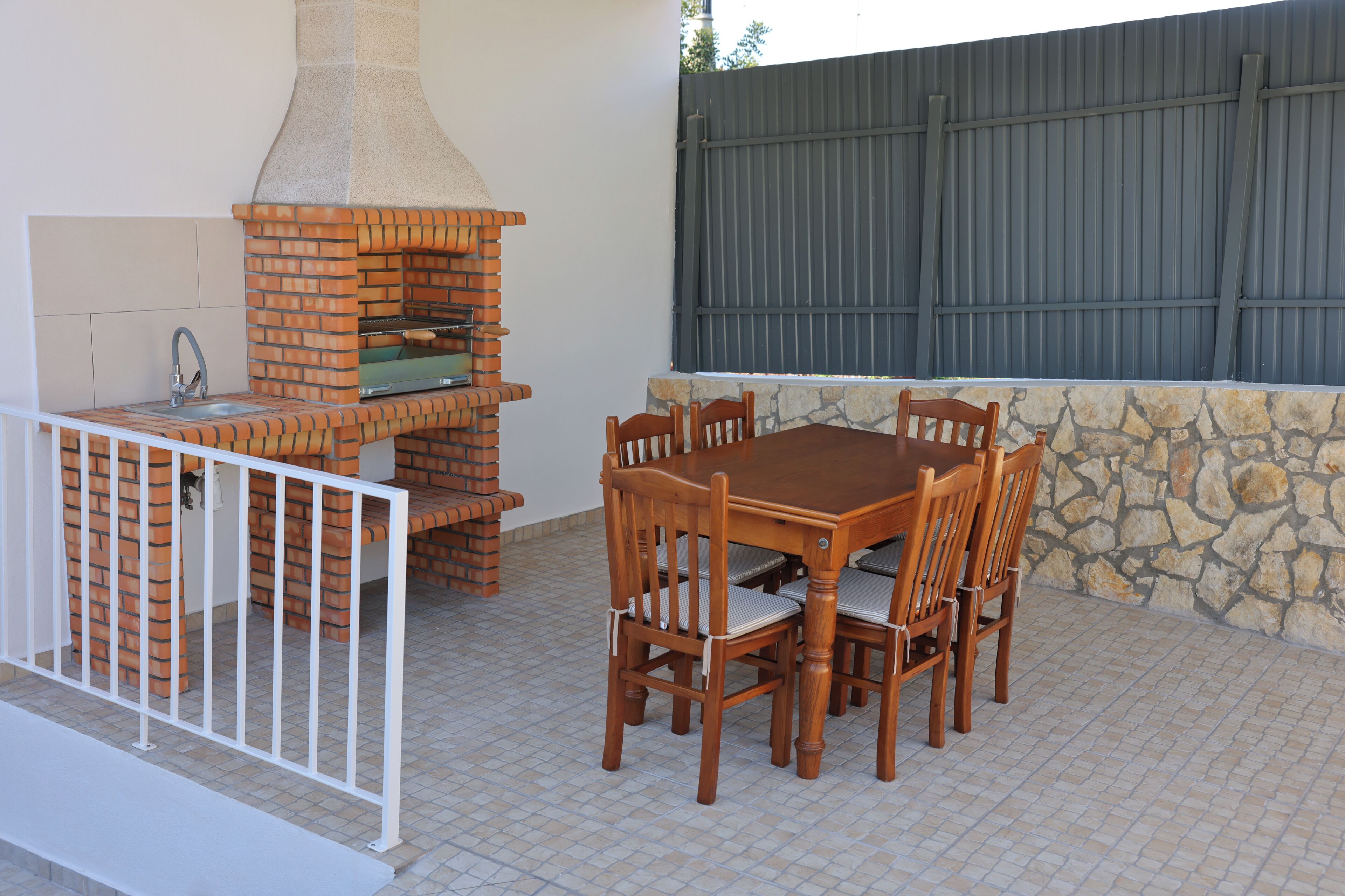 Une terrasse extérieure avec un four en briques, un mur en pierre et une table entourée de chaises.