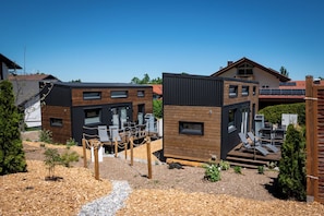 A modern two-story house with a deck, outdoor seating, and a clear sky.