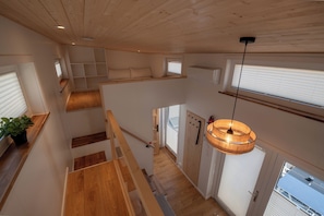 Un interior con varios niveles, pisos de madera, una escalera, una lámpara colgante y una vista por la ventana.