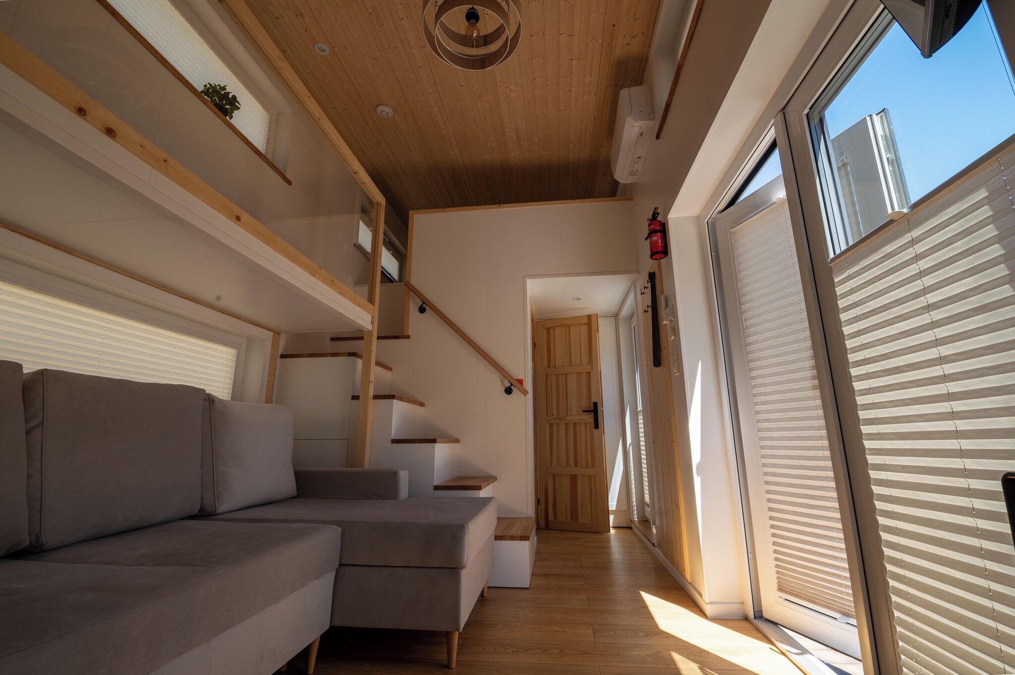 Un intérieur moderne avec un canapé d’angle gris, un escalier en bois et de grandes portes-fenêtres coulissantes.