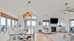 A spacious living area with a dining table, chairs, a sofa, a fireplace, and a television. - Walk to Beach | Sunset Views! Pool | Hot Tub| Duck (Duck)