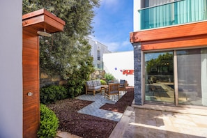 Un patio moderno al aire libre con una pérgola de madera, un muro de piedra y una zona de estar con mesa y sillas.