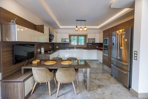 Una cocina moderna con un refrigerador grande, una mesa de comedor con sillas y un televisor montado en la pared.