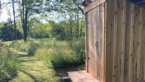 Un cobertizo de madera con una puerta y una pequeña plataforma de madera.