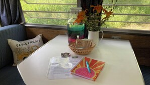 Una mesa pequeña con una cesta, un florero con flores, una botella de agua y un cuaderno con un bolígrafo.