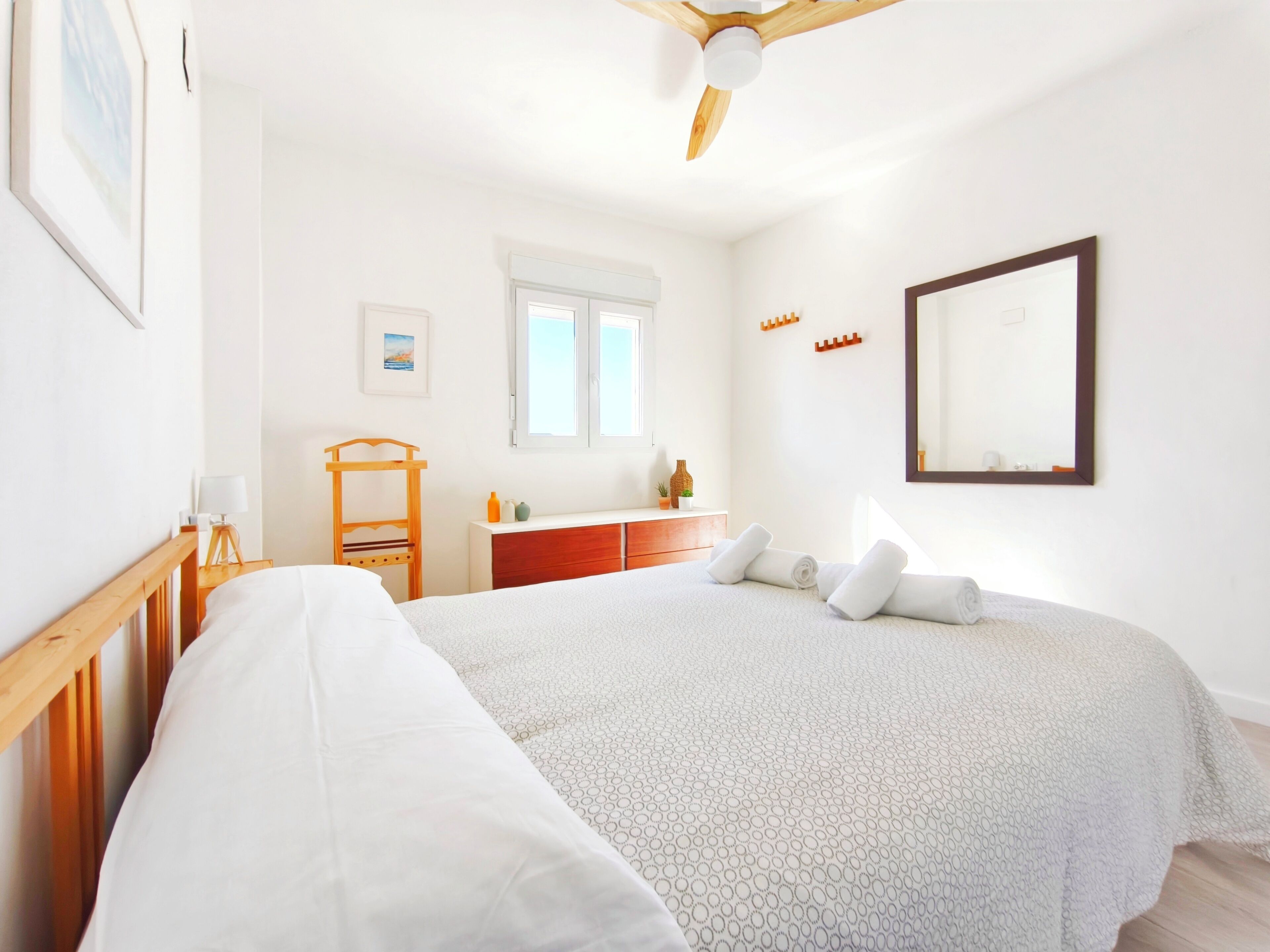 A bedroom with a bed, a wooden headboard, a dresser, a mirror, and a ceiling fan.