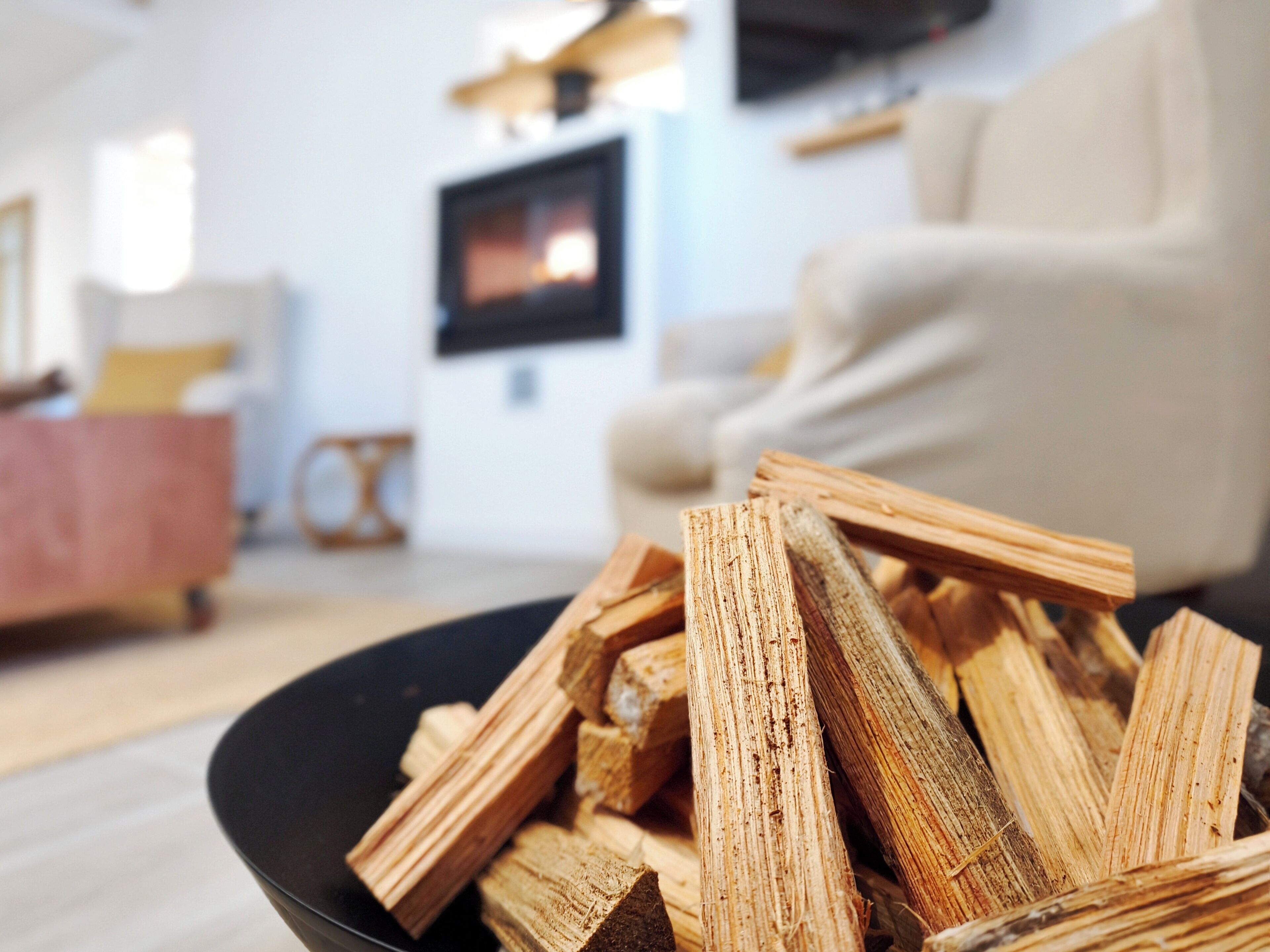 Ein Zimmer mit einer schwarzen Schüssel voller Brennholz, einem an der Wand montierten Fernseher und einem beigen Sessel.