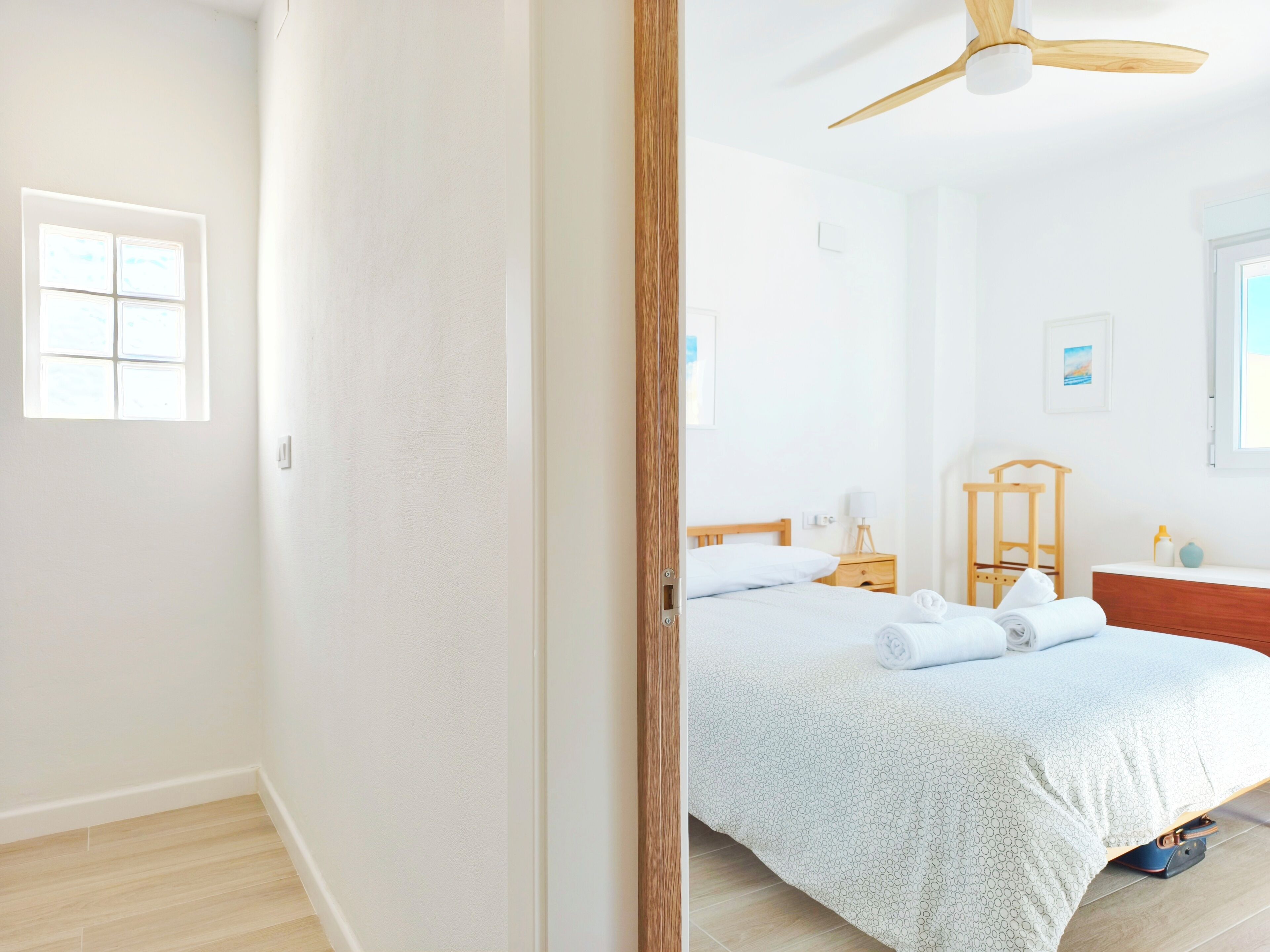 Ein Schlafzimmer mit Bett, Nachttisch, Lampe, Holz-Kopfstück und Deckenventilator.