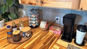 A kitchen counter with a coffee maker, a mug, a jar of coffee beans, a spice rack, and a plant.