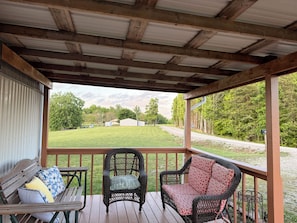 A covered porch with wicker furniture and a view of a green landscape. - Betty Gap Getaway - Close to Red River Gorge & Cave Run Lake (Wellington)