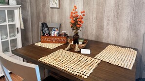 A wooden dining table with placemats, a vase with orange flowers, a wooden box labeled 'S'MORES Station,' and a cabinet with dishes.