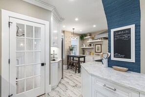A kitchen with white cabinetry, a marble countertop, and a chalkboard with a motivational quote. - Historic Luxury Meets Modern Living — 6BR Victorian in the Heart of Newport (Newport)