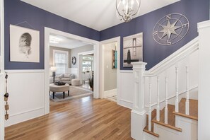 A hallway with wooden flooring, a white staircase, and a compass wall decoration. - Historic Luxury Meets Modern Living — 6BR Victorian in the Heart of Newport (Newport)