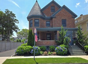 Una casa a due piani in mattoni con tetto a falde, un portico e un palo con la bandiera americana.