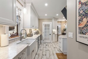 A modern kitchen with white cabinetry, a marble countertop, and a farmhouse-style floor. - Historic Luxury Meets Modern Living — 6BR Victorian in the Heart of Newport (Newport)