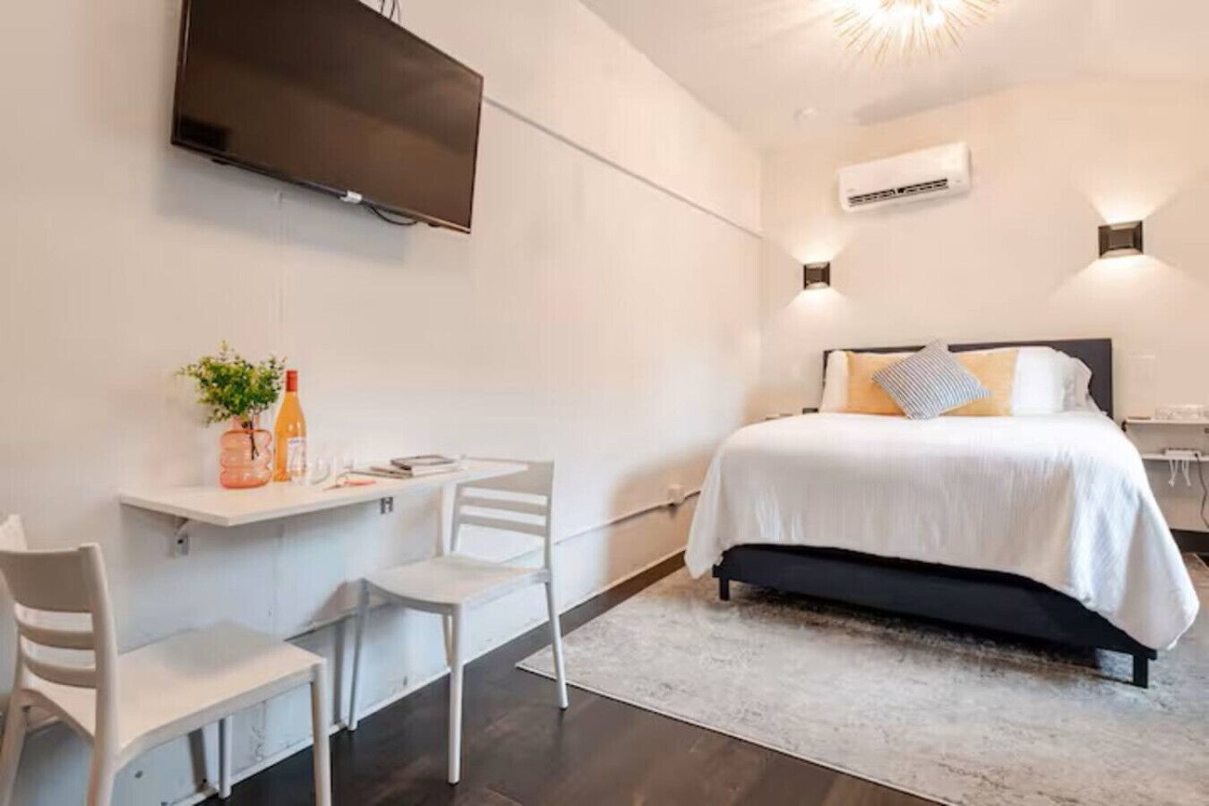 Ein modernes Hotelzimmer mit einem Bett, einem Schreibtisch mit Stühlen, einem Fernseher und einer Klimaanlage.