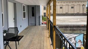 Un balcon abrité avec un plancher en bois, une chaise en métal noir et une vue sur un bâtiment situé de l’autre côté d’une étendue d’eau.