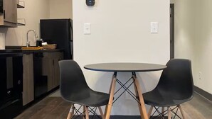 Une cuisine moderne avec des meubles de couleur sombre, un réfrigérateur noir et une table de salle à manger ronde, accompagnée de deux chaises noires.